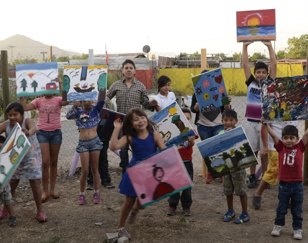 Alejandro y un grupo de niños muestran con alegría las pinturas que hicieron en el taller